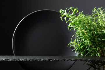 Black stone podium, black ceramic plate and branches of rosemary.
