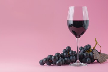 Elegant Red Wine Glass with Black Grapes on Pink Background