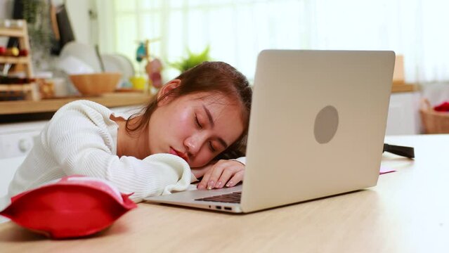 bored Tired exhausted, fatigue and fell asleep. Yaoung asian thai female working on laptop in kitchen room at home. Overwork. Exhausted woman  sleeply eye at workplace