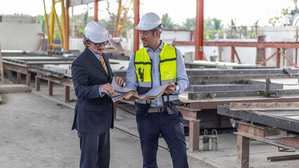 Two civil engineers checking information from file and tablet for quality control in a precast or...