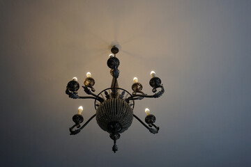 Old artistic chandelier with electric candles on the ceiling