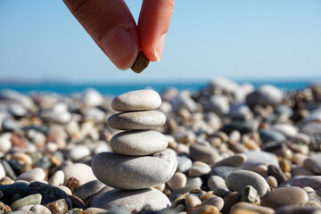 Balance of mind - abstract - hand putting pebble on the tower of stones on the sunny beach
