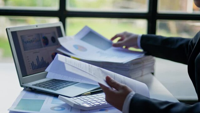 Businessman is seriously stressed working on laptop and document paperwork and headache due to office syndrome on laptop and paperwork in the office.