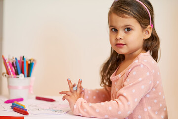 Portrait, girl and colouring at home, desk and crayons for development, activity and art. Child, drawing and education for paper, book and preschooler with picture, creative homework and kindergarten
