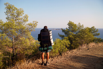 A man in shorts with a backpack, tourist mat, tent and a solar panel on it looks at the islands in...