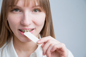 Young woman with metal braces on her teeth is chewing gum. Copy space. 