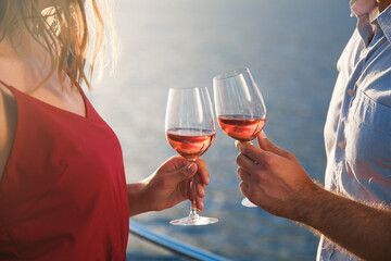 Drinking wine by sea. Two wineglasses in hands of couple in love at sunset beach. Man and woman...