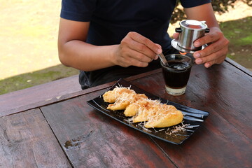 a man is enjoying Vietnamese style coffee with fried banana in an outdoor cafe