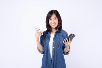 Asian woman wearing denim jean is holding dollar and a mobile phone against a white background,...