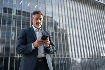 Mature hispanic senior business man using smartphone cellphone at office building. Focused serious...