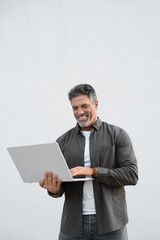Mature smiling man using wireless pc for business solutions, isolated on white background. Middle age freelance entrepreneur, latin hispanic businessman holding laptop computer, working busy. Vertical