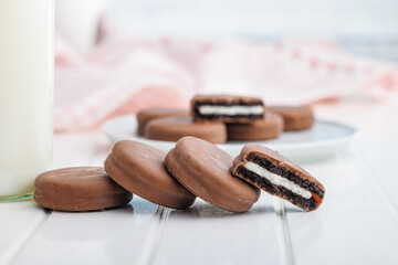 Chocolate Covered Cookies and Glass of Milk on white table. - obrazy, fototapety, plakaty