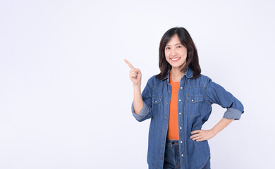 A Young asian woman wearing orange t shirt and denim jean while pointing finger to free copy space...
