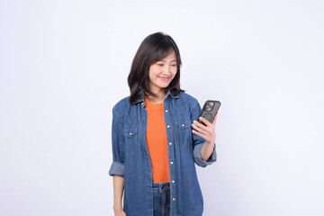 Asian woman wearing an orange shirt and a denim jacket is celebrating the news on mobile phone...