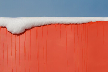 Melting snow on colourful bright red metal wall abstract background