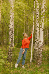 a girl in blue jeans and an orange jumper among birch trees, taken on a cloudy spring day in the village of Shanary in Chuvashia