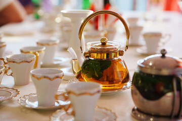Classic white and gold tea set and glass teapot on the served table. Dishes for tea drinking.