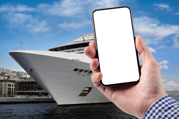 A man holds a smartphone in his hand. Cruise liner stands on the pier.