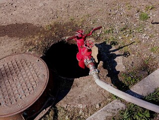 A red fire hydrant is installed on a hydrant in a sanitary well. Water supply from a fire hydrant using fire hoses.