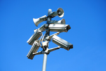 A pole on the street with cameras and loudspeakers mounted on it against a blue sky background.