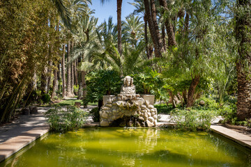 Pond of water and palm trees with the image of the Lady of Elche in the Huerto del Cura in Elche,...