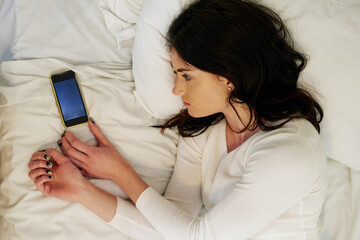 Tired, woman and smartphone in bed from break up with depression, anxiety and insomnia at home....