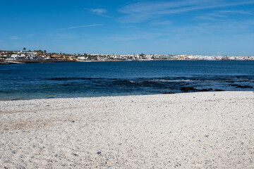 Walking on sea promenade in Corralejo along white popcorn beach with white corals, black rocks, blue water, Fuerteventura, Canary islands, Spain