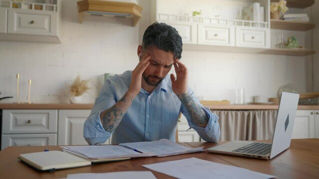Depressed desperate man doing paperwork. Stressed tired worried businessman working with laptop at home looking at paying bills in finance, looking frustrated. Money debt, budget, pressure concept.