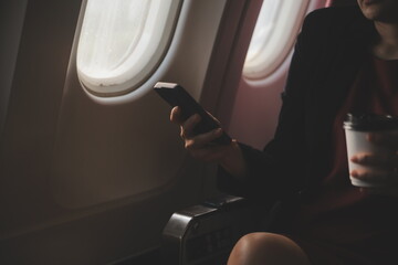 Blonde female tourist checking incoming notification on smartphone sitting on seat of airplane with netbook.Young businesswoman share media from telephone on laptop computer during plane flight