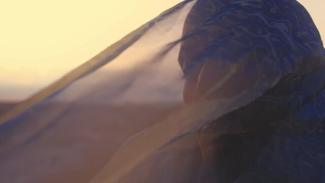 Woman with shaved head sitting in the desert with scarf