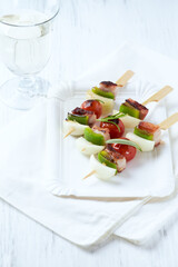 Shashlik with bacon, cherry tomato and green pepper. Bright wooden background. Close up. Copy space.