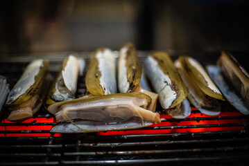 Grilled razor clams on a charcoal grill for sale to tourists at the Ban Na Kluea Seafood Market, Thailand.