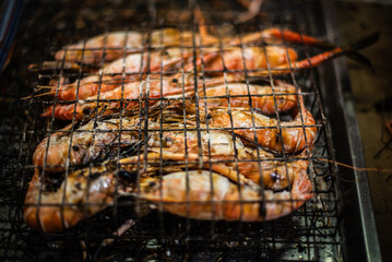 River prawns are placed on a metal griddle and grilled over a charcoal grill for sale to tourists at the Ban Na Kluea Seafood Market, Thailand.
