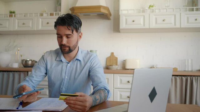 Man online paying credit card on phone. Businessman concentrated working on laptop, paying mobile phone money finances shopping ecommerce enter secure code safe transaction at home. Online paying.