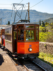 The Tramvia de Sóller tram traverses the lush gardens of Sóller, passing by the Roca Roja station en route to Port de Sóller town, offering travelers a glimpse of Mallorca heritage and scenic beauty.