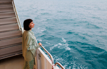 young woman stands on the deck of a cruise ship and looks at the setting sun, close-up silhouette. A young beautiful brunette travels on a yacht.