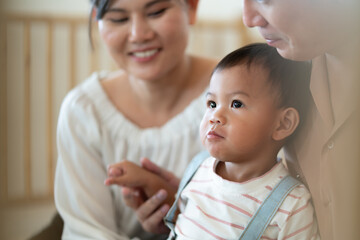 Fototapeta premium Warm moment of an Asian couple with their toddler in a softly lit room, reflecting family happiness and bonding.