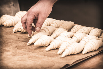 Baker puts raw croissants on a baking tray, prepared for baking. Vintage style with grain.