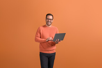Portrait of happy confident businessman checking e-mails over wireless computer on orange background