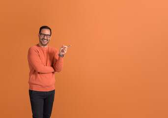 Portrait of happy salesman pointing at copy space and demonstrating new product on orange background