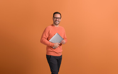 Portrait of confident male professional holding wireless computer and smiling on orange background