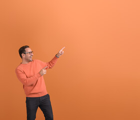 Excited young man pointing aside at copy space and demonstrating new product on orange background