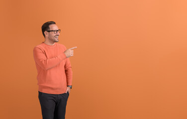 Young cheerful salesman pointing and presenting new product on copy space over orange background