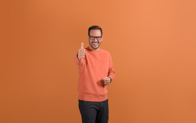 Portrait of positive young businessman smiling and gesturing thumbs up on isolated orange background