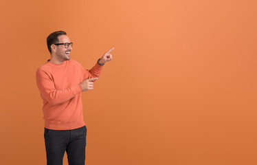 Cheerful young businessman pointing at copy space and promoting new business on orange background