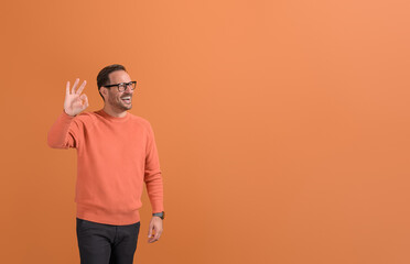 Cheerful male professional laughing and looking away while showing OK sign on orange background