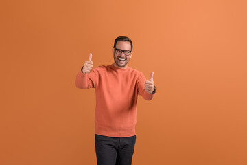 Portrait of ecstatic young man showing thumbs up sign with both hands on isolated orange background