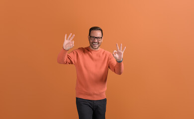 Portrait of handsome entrepreneur in glasses smiling and showing OK sign against orange background
