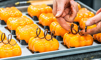 Confectioner's hand decorating orange glazed tartlets with chocolate