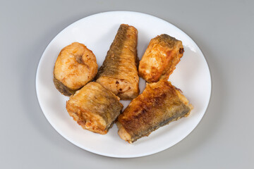 Fried Argentine hake pieces on white dish on gray background